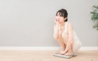 Eine dünne Frau kniet nachdenklich auf einer Wage