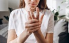 Frau haelt sich schmerzend die Hand.