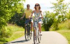 Mann und Frau fahren laechelnd Fahrrad im Gruenen.