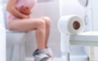Eine sitzende Frau mit Bauchschmerzen auf der Toilette.