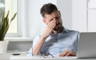 Mann reibt sich muede die Augen am Schreibtisch.