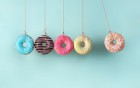 Fünf bunte Donuts hängen an roten Schnüren vor einem hellblauen Hintergrund.