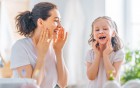 Mutter und Kind tragen gemeinsam Hautcreme auf und lachen im Badezimmer.