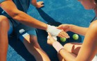 Person verbindet die Hand einer verletzten Sportlerin auf einem Tennisplatz.