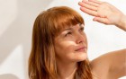 Eine rothaarige Frau blickt nach oben in die Sonne und schützt ihre Augen mit einer Hand vor dem hellen Licht.