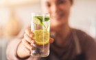 Eine Person hält ein erfrischendes Glas Wasser mit Zitronen- und Gurkenscheiben direkt in die Kamera.